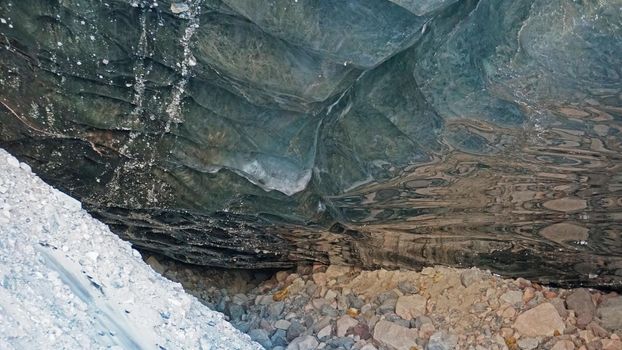 Ice cave in the snowy mountains. Tuyuk-Su glacier. Black ice reflects everything like a mirror. The ledge of stones collapsed. huge cracks in the ice tunnel. Snowy mountains of Almaty, Kazakhstan.