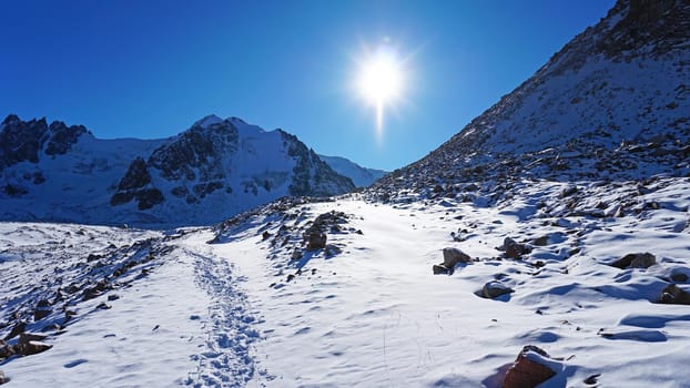 High rocks covered with snow. The Tuyuk Su Glacier. The view from the drone to the tops of the peaks. Completely surrounded by winter mountains. blue clear sky and bright sun. Shadows from mountains