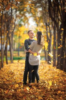 Young caucasian couple whirl in dance in autumn park under autumn leaf fall.