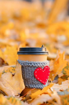 Paper coffee cozy cup with heart shape in autumn leaves, vertical copy space.
