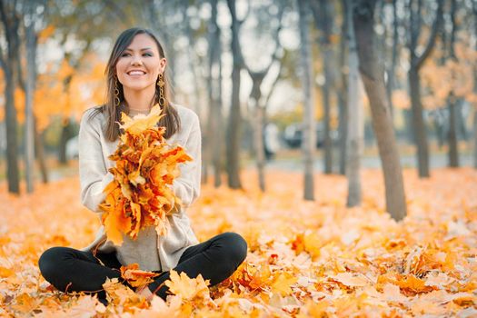 Satisfied smiling young woman having fun in autumn park playing with fallen leaves, copy space.