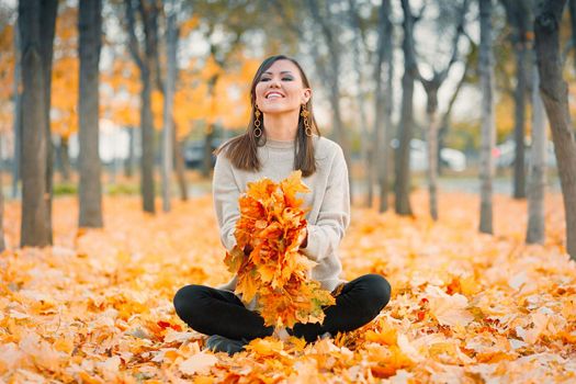 Satisfied smiling young mixed race woman having fun in autumn park playing with fallen leaves.