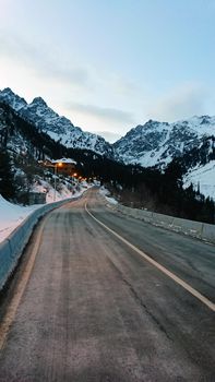The building of the snowy mountains and forests. Dawn. Lanterns are lit, the road goes into the gorge. The high peaks are completely covered with snow. Almaty, Shymbulak ski resort, Kazakhstan.