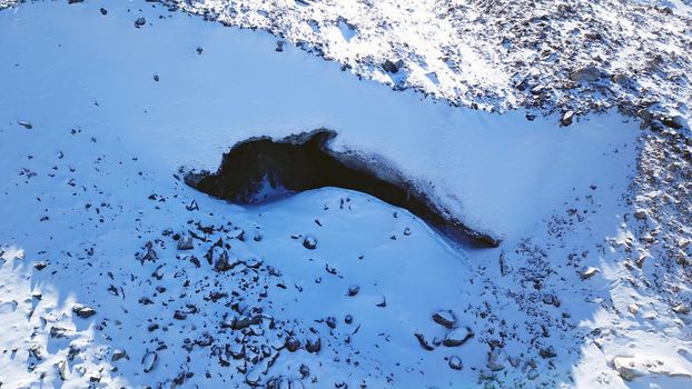 Entrance to an ice cave in the mountains. Tuyuk Su Glacier, all covered in white snow. You can see an ice grotto covered with ice and rocks. High rocks and mountains. The entrance looks like a dolphin