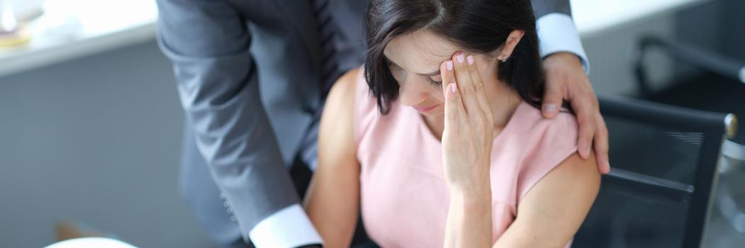 Businessman hugs embarrassed employee in office. Sexual harassment at work concept