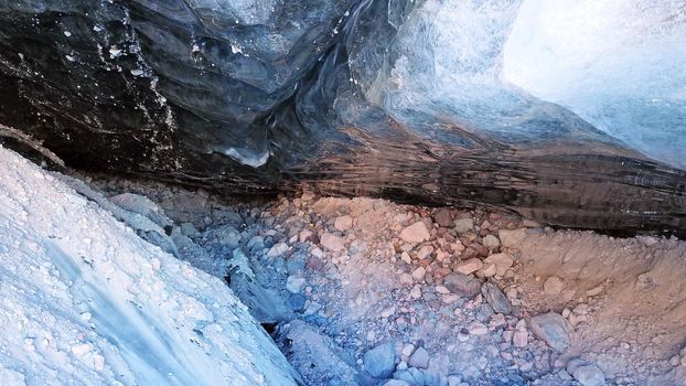 Ice cave in the snowy mountains. Tuyuk-Su glacier. Black ice reflects everything like a mirror. The ledge of stones collapsed. huge cracks in the ice tunnel. Snowy mountains of Almaty, Kazakhstan.