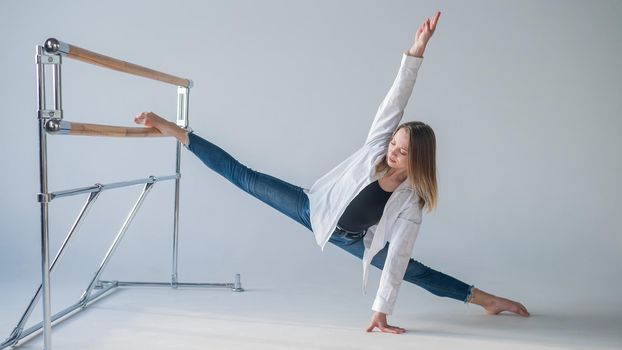 Caucasian woman in casual clothes pulls the split at the ballet barre