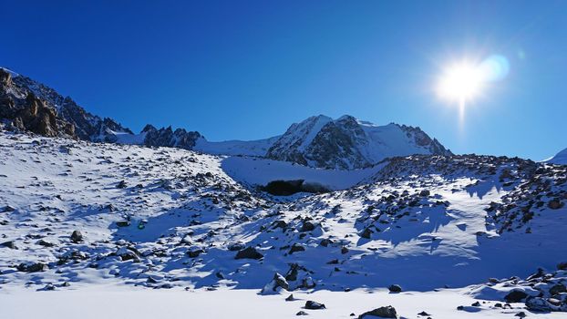 Entrance to an ice cave in the mountains. Tuyuk Su Glacier, all covered in white snow. You can see an ice grotto covered with ice and rocks. High rocks and mountains. The entrance looks like a dolphin