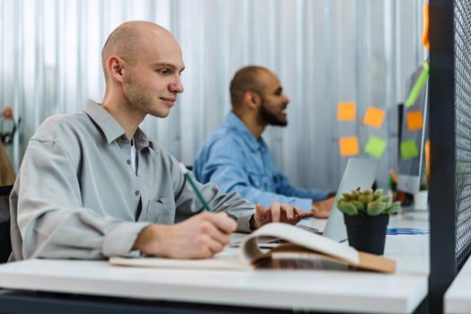 Young bald business man sitting at desk in office, working on computer, close up