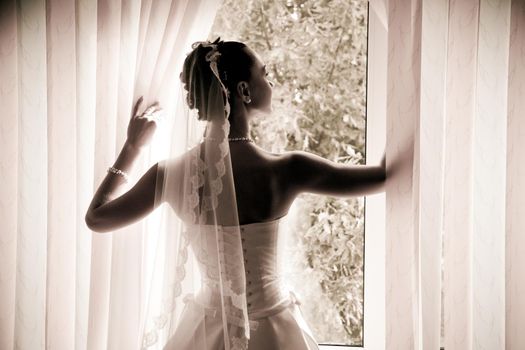 Woman in a wedding gown stands in front of a window.