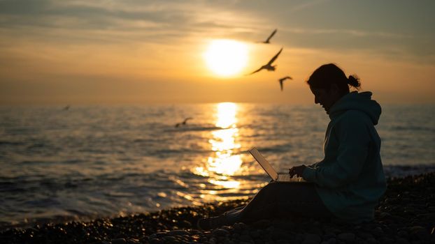 Caucasian woman typing on a laptop on the seashore at sunset. Freelance work