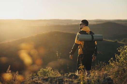 Back View of One Travel Man with Backpack with Camping Mat, Standing on Top of Hill During Sunset, Male Nomad Enjoy His Solo Trip