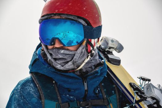 Closeup portrait of ski goggles of a man with reflection of snowy mountains. The mountain range is reflected in the ski mask. Portrait of a man in a ski resort against the backdrop of mountains and sky in a snow blizzard.