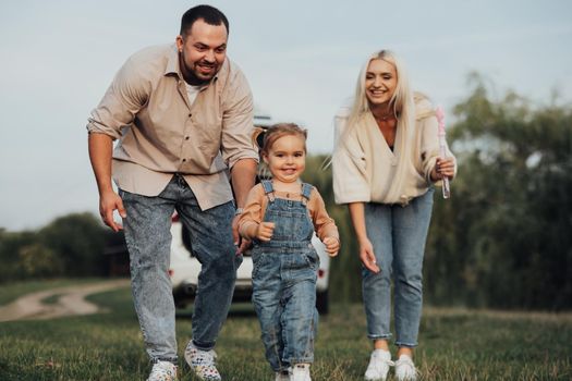 Happy Young Family Having Fun Outdoors, Little Daughter Playing Running Away from Her Parents