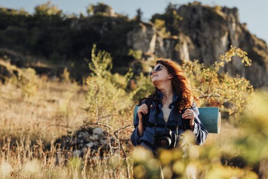 Young Traveler Woman in Sunglasses with a Digital Camera and Backpack with Camping Mat Standing Against Mountain, Female Hiker Enjoy Freedom on Her Solo Trip