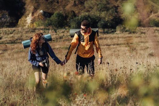 Man and Woman Holding by Hands While Hiking Together on Hill During Sunset, Young Couple Enjoy Their Trip with Backpacks and Camping Mat