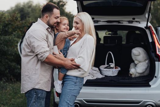 Young Parents with Their Toddler Daughter Hugging in front of SUV Car, Family Enjoying Road Trip Weekend