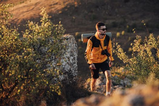 Male Hiker with Backpack and Digital Camera Walking on Hill During Sunset, Traveler Man in Solo Trip