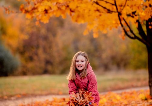Preteen girl kid holding yellow fallen leaves in hands and smilng at autumn park. Beautiful portrait of child outdoors at nature