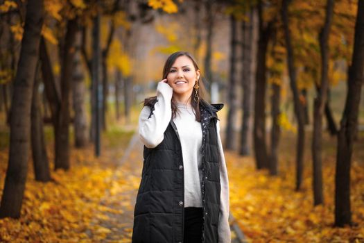 Portrait of a young woman in the Almaty autumn park on the alley with fallen autumn leaves.