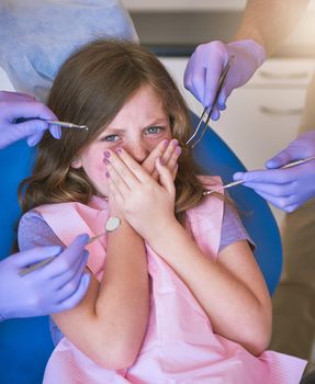 Shot of a little girl looking terrified as dentists get ready to examine her.