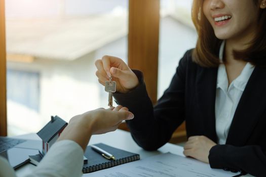 Accountant, businessman, real estate agent, Asian business woman handing keys to customers along with house after customers to sign.