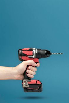 Cordless screwdriver in hand. Cordless tool in a man's hand. The concept of repair and construction on a blue background