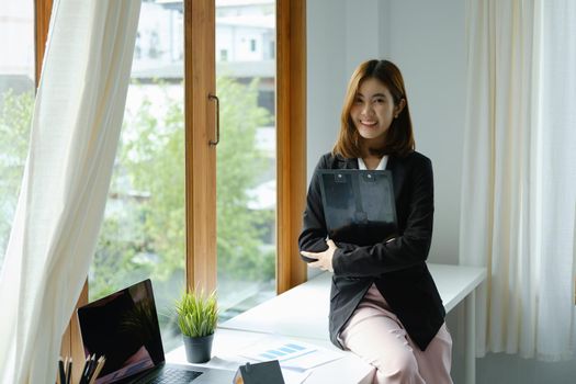 Portrait of a smiling Asian businesswoman holding job analysis and financial and marketing documents.