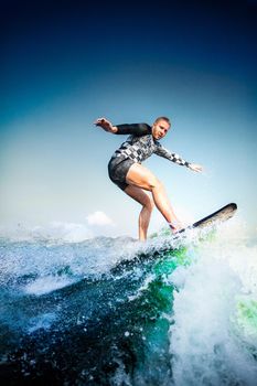 Surfing at blue sea. Young man balanced on wave on surfboard. Wake surf outdoor lifestyle.