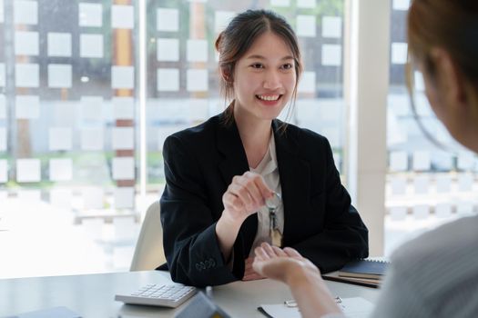 Accountant, businessman, real estate agent, Asian business woman handing keys to customers along with house after customers to sign.