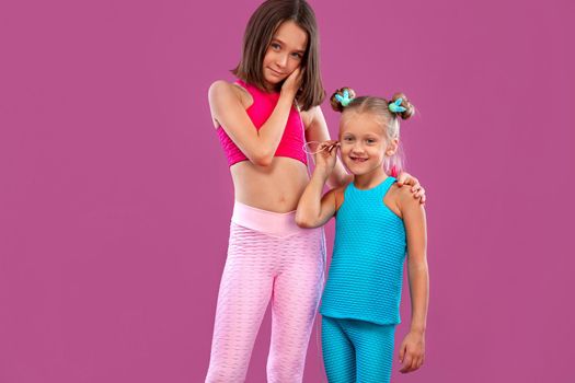 Two children girls listen to music on a pink background. Kids lifestyle concept. Sportswear for kids.