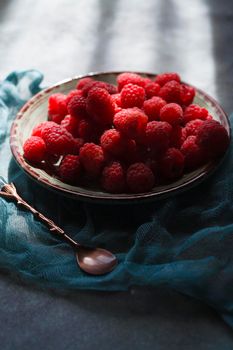 Red raspberry on green plate with blue cloth and small vintage spoon, selective focus.