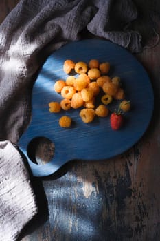 Yellow raspberry on blue kitchen board on wooden table, top view.