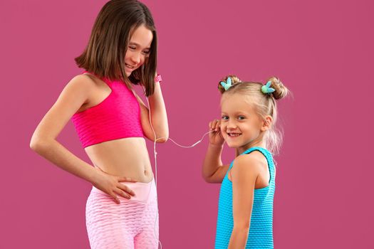 Two children girls listen to music on a pink background. Kids lifestyle concept. Sportswear for kids.