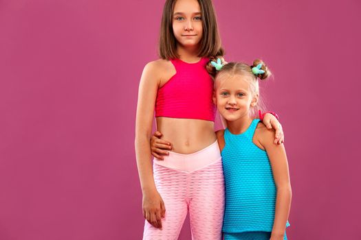 Two children girls listen to music on a pink background. Kids lifestyle concept. Sportswear for kids.