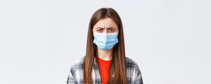 Coronavirus outbreak, leisure on quarantine, social distancing and emotions concept. Close-up of bothered or displeased woman in medical mask, condemn someone, frowning upset.