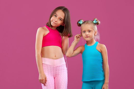 Two children girls listen to music on a pink background. Kids lifestyle concept. Sportswear for kids.
