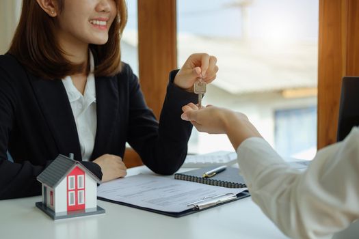 Accountant, businessman, real estate agent, Asian business woman handing keys to customers along with house after customers to sign.