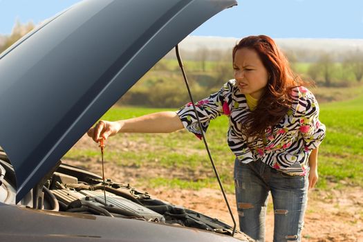 young woman with oil probe bent over car engine