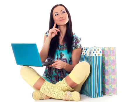 Beautiful young woman sitting on the floor with laptop and paper bags and doing online shopping.