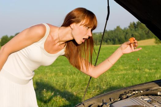 young woman with oil probe bent over car engine