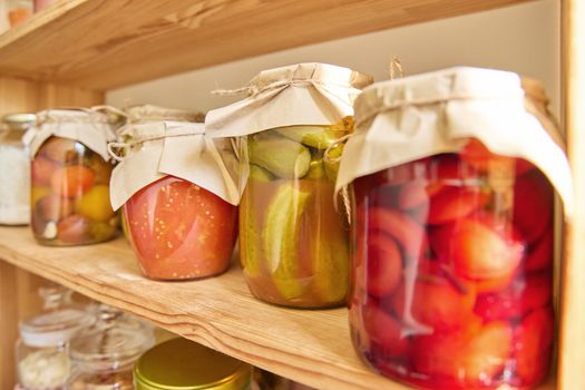 Storage of food in the kitchen in pantry. Pickled canned vegetables and fruits on the shelf, jar of cucumbers close-up. Cooking at home, homemade preservation, household