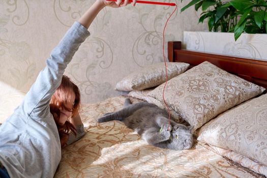 Preteen girl playing with a pet gray british cat lie together at home in bed. Animals, children, friendship care and love concept
