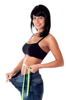 Pretty brunette girl holding her pants open and showing with a measuring tape around her waist how much centimeters she has already lost. Isolated on white.