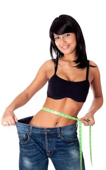 Pretty brunette girl holding her pants open and showing with a measuring tape around her waist how much centimeters she has already lost. Isolated on white.