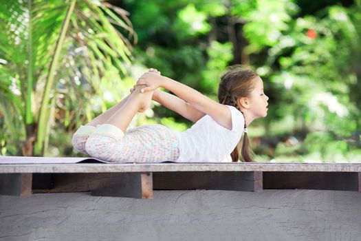 Child doing exercise on wooden platform outdoors. Healthy lifestyle. Yoga girl