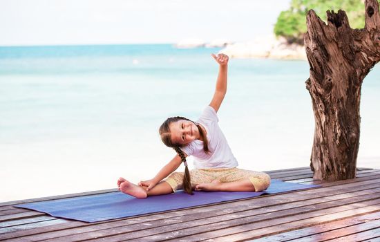 Child doing meditating exercise on wooden platform sea shore outdoors. Healthy lifestyle. Yoga girl