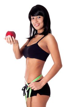 Pretty brunette girl holding apple and showing with a measuring tape around her waist how much centimeters she has already lost. Isolated on white.