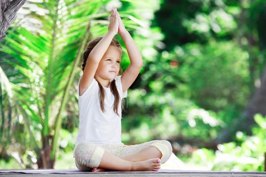 Child doing exercise on wooden platform outdoors. Healthy lifestyle. Yoga girl