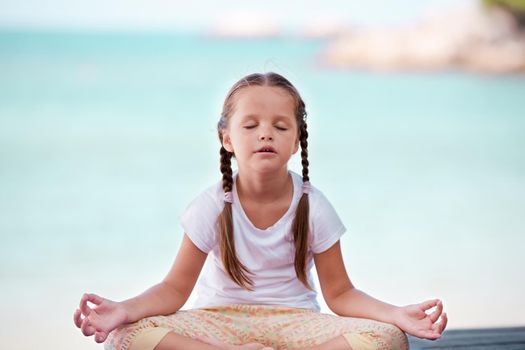 Child doing meditating exercise on wooden platform sea shore outdoors. Healthy lifestyle. Yoga girl